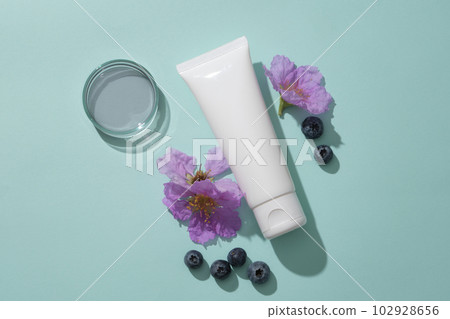 Minimal backdrop for cosmetic branding presentation - white plastic tube unlabeled container cleanser or cream, blueberries and purple flowers decorated on blue background. 102928656