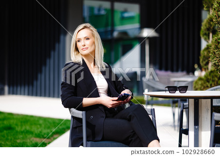 Blonde business lady looks at the phone, reading messages. Woman is relaxing in a cafe on the terrace enjoyment of life 102928660