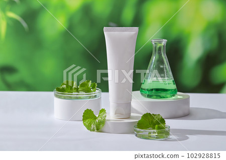 Unlabeled cosmetic container and an erlenmeyer flask of green liquid placed on round white podiums. Gotu kola (Centella asiatica) is widely used in skin care Unlabeled cosmetic container and an erlenmeyer flask of green liquid placed on round white podiums. Gotu kola (Centella asiatica) is widely used in skin care 102928815