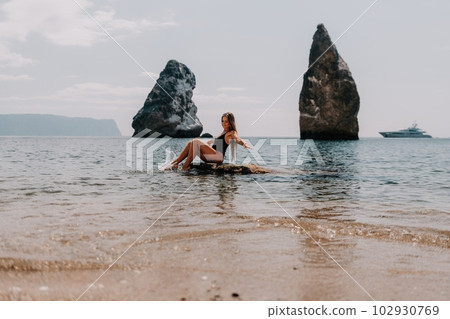 Woman summer travel sea. Happy tourist enjoy taking picture outdoors for memories. Woman traveler posing on the beach at sea surrounded by volcanic mountains, sharing travel adventure journey Woman summer travel sea. Happy tourist enjoy taking picture outdoors for memories. Woman traveler posing on the beach at sea surrounded by volcanic mountains, sharing travel adventure journey 102930769