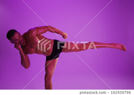 Man athletic bodybuilder poses with nude torso abs in full-length background, boxing and martial arts. Advertising, sports, active lifestyle, color light, competition, challenge concept.  102930798