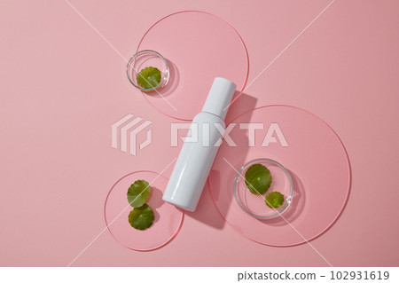 Top view of white bottle displayed on pink background with gotu kola in petri dish and acrylic sheets. Blank label for branding mockup, gotu kola extract, skincare beauty product concept. 102931619