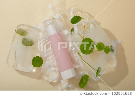 Advertising scene for cosmetic product with pink bottle unlabeled placed on ice cubes with frozen gotu kola leaves inside on beige background. Mockup, copy space 102931638
