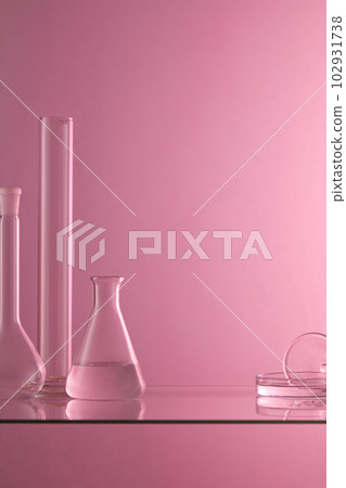 Several laboratory glassware containing transparent liquid are placed on a glass table with purple background. Blank space to display product 102931738