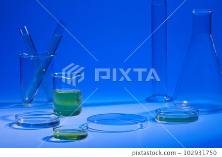 Beaker and petri dish of yellow liquid displayed with other laboratory glassware on a blue background. Vacant space on podium 102931750