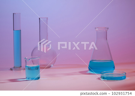 Several glassware containing blue liquid against a gradient background. Cosmetic laboratory research and development Several glassware containing blue liquid against a gradient background. Cosmetic laboratory research and development 102931754