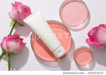 Scene for branding cosmetic of rose extract, plastic tube unlabeled for design placed on petri dish containing pink liquid and fresh roses arranged on white background Scene for branding cosmetic of rose extract, plastic tube unlabeled for design placed on petri dish containing pink liquid and fresh roses arranged on white background 102932515