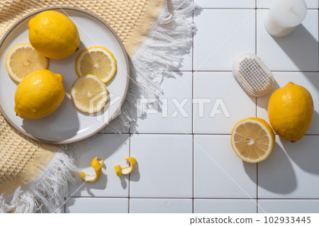 A dish of Lemon slices placed on a wool scarf decorated with candle and a scrub brush. Blank space for product presentation. Copy space. The benefits of Lemon (Citrus limon) for skin are numerous 102933445