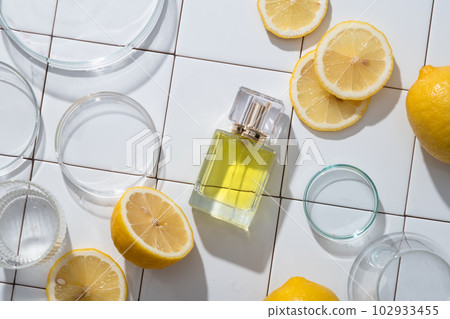Glass transparent bottle of perfume extracted from Lemon essential oil arranged with petri dishes and Lemon slices. Lemon (Citrus limon) can be used in perfume production 102933455