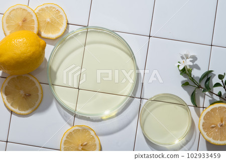 Two glass petri dishes filled with essential oil extracted from Lemon on a mosaic tiles background. The citric acid found in Lemon (Citrus limon) brightens your skin 102933459