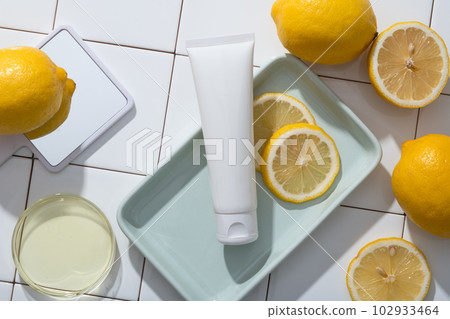 A hand mirror, a petri dish of Lemon essential oil and a tray of white tube and Lemon slices are decorated on mosaic tiles background. Lemon (Citrus limon) has antifungal and antimicrobial properties 102933464