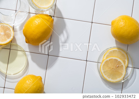Glass petri dishes with Lemon slices placed on and filled with essential oil extracted from Lemon (Citrus limon). Blank space in the middle for natural cosmetic product presentation 102933472
