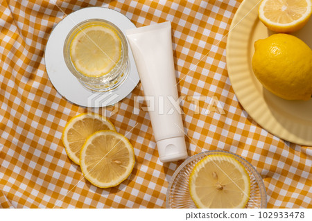 A cosmetic container without label decorated with mirror, glasses with Lemon slices and a dish of lemons. Lemon (Citrus limon) helps control acne-causing bacteria 102933478