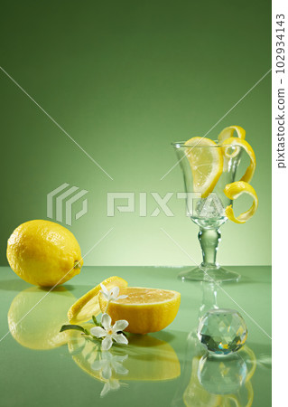 Fresh lemon, slices and peel of lemon decorated with glass cup and crystal ball on backlit green background. Minimal concept, space for cosmetic product presentation Fresh lemon, slices and peel of lemon decorated with glass cup and crystal ball on backlit green background. Minimal concept, space for cosmetic product presentation 102934143