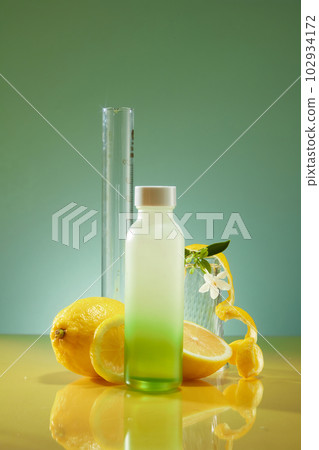 A gradient glass bottle unbranded decorated on backlit background with peel and halves of lemon, white flower. Mockup for product with lemon ingredient, fresh lemon flavored drink A gradient glass bottle unbranded decorated on backlit background with peel and halves of lemon, white flower. Mockup for product with lemon ingredient, fresh lemon flavored drink 102934172