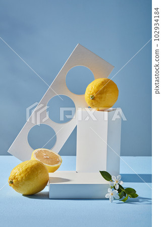Fresh lemons on blue background with white geometric cylinders and branch flower. Pedestal for cosmetic product and packaging mockups display presentation. Natural organic extract with vitamin C Fresh lemons on blue background with white geometric cylinders and branch flower. Pedestal for cosmetic product and packaging mockups display presentation. Natural organic extract with vitamin C 102934184