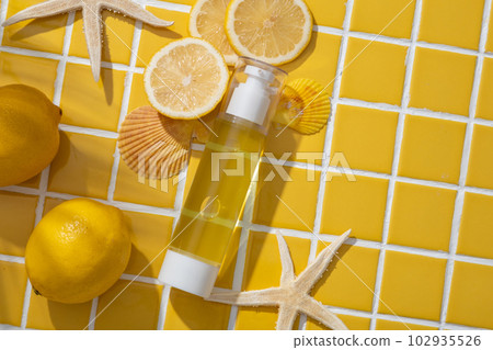 Over a mosaic tiles background, a blank label transparent bottle filled with yellow liquid displayed with seashells, starfishes and Lemon slices. Lemon can keep your skin firm and strong 102935526