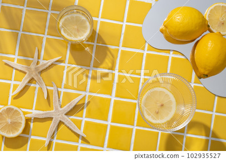 Lemon placed on a mirror arranged with starfishes and two glasses containing Lemon slices. Vacant space on the yellow mosaic tiles background to show natural cosmetic product Lemon placed on a mirror arranged with starfishes and two glasses containing Lemon slices. Vacant space on the yellow mosaic tiles background to show natural cosmetic product 102935527
