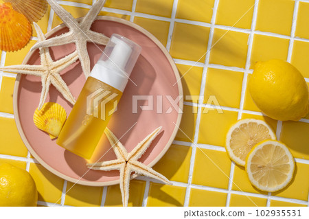 A round pink dish with starfishes, seashells and unlabeled transparent bottle of essential oil extracted from Lemon placed on. Cosmetics, products for care and personal hygiene concept 102935531