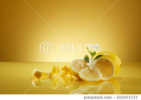 Some Lemon slices and peels decorated on mirror table with small white flowers against a yellow background. Lemon (Citrus limon) is known as a natural skin brightener 102935533