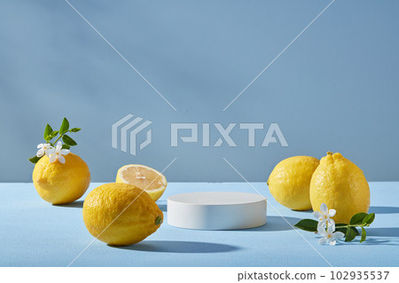 Minimal scene of a white podium in round shape decorated with several Lemons and small white flowers with front view. Light blue background. Organic product promotion of Lemon (Citrus limon) extract 102935537