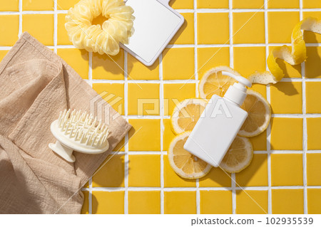 Unbranded pump bottle dispenser placed on some Lemon slices, displayed with hair tier, mirror and scalp massage brush on towel. Mockup of skin care cosmetic tube of beauty facial 102935539