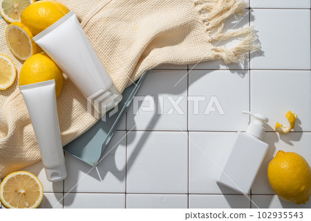 Over a mosaic tiles background, two white tubes and beige wool scarf are put on a tray, arranged with a pump bottle. Citric acid in Lemon (Citrus limon) can help break down dead skin cells 102935543
