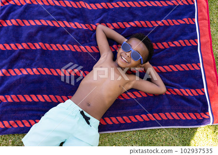 African american shirtless boy with hands behind head wearing sunglasses and lying on towel 102937535