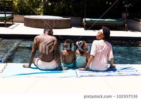 Rear view of african american parents and children sitting at poolside at resort on sunny day Rear view of african american parents and children sitting at poolside at resort on sunny day 102937536
