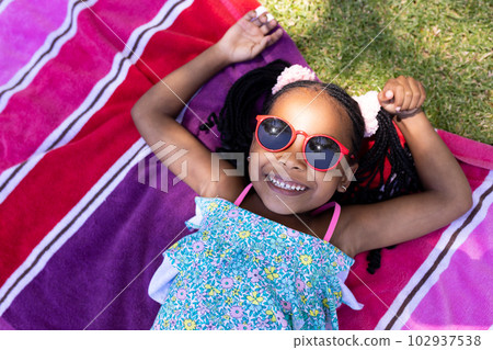 High angle view of cute african american girl wearing sunglasses lying on towel High angle view of cute african american girl wearing sunglasses lying on towel 102937538