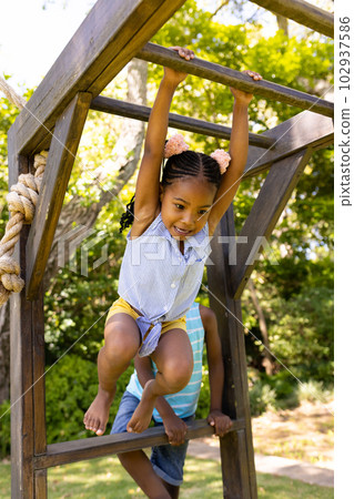 Low angle view of african american girl hanging on monkeys bars at playground 102937586