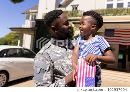 African american army soldier carrying son holding flag of america and standing outside house African american army soldier carrying son holding flag of america and standing outside house 102937604