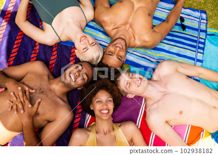 Happy diverse group of friends lying on towels and smiling with eyes closed in garden 102938182