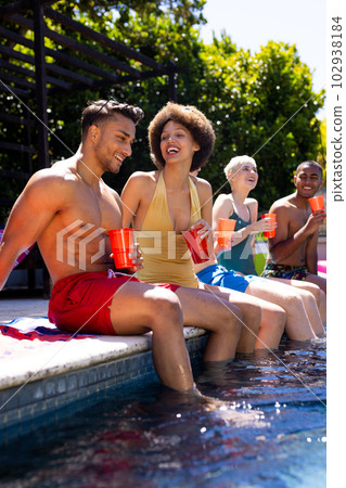 Happy diverse group of friends having pool party, holding plastic cups in garden 102938184