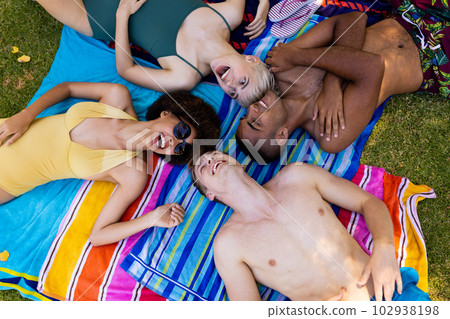 Happy diverse group of friends lying on towels and laughing in garden 102938198