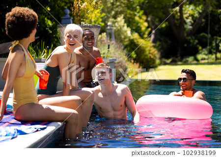 Happy diverse group of friends having pool party, holding plastic cups in garden 102938199