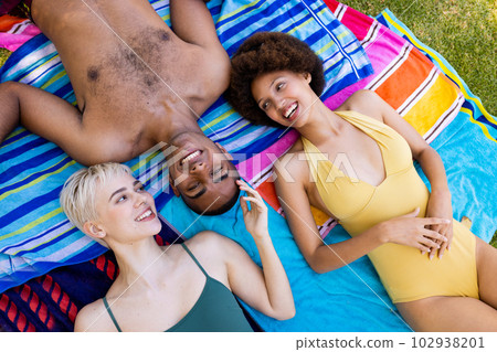 Happy diverse group of friends lying on towels and smiling in garden Happy diverse group of friends lying on towels and smiling in garden 102938201