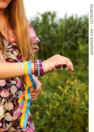 Ukraine flag. Girl wind patriotic ribbon or tape on her hand. Many bracelets. Summer outside. Vertical. Freedom, peace concept 102939050