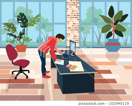 A male employee in the office stands over a table with a laptop and documents. Office landscaping. Bright room for workshop. Freelancer workplace at home. 102940119