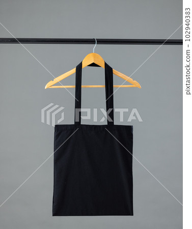 Close up of black canvas bag hanging on wooden clothes hanger with copy space on grey background Close up of black canvas bag hanging on wooden clothes hanger with copy space on grey background 102940383