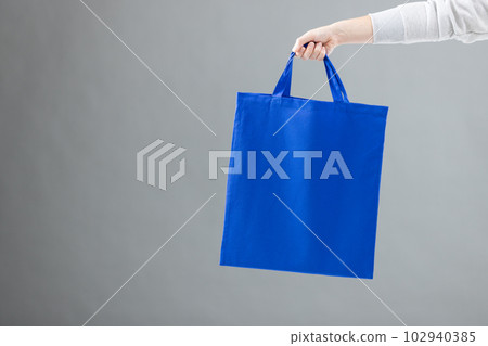Hand of caucasian woman holding blue canvas bag with copy space on grey background Hand of caucasian woman holding blue canvas bag with copy space on grey background 102940385