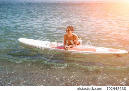 Woman sup sea travel. Sports girl on a surfboard in the sea on a sunny summer day. In a black bathing suit, he sits on a sapa in the sea. Rest on the sea. Woman sup sea travel. Sports girl on a surfboard in the sea on a sunny summer day. In a black bathing suit, he sits on a sapa in the sea. Rest on the sea. 102942688