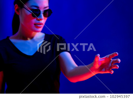 Asian woman with glasses making gesture with hand in studio with blue light with copy space 102945397