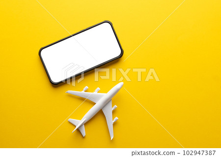 Close up of white airplane model and smartphone with copy space on screen on yellow background Close up of white airplane model and smartphone with copy space on screen on yellow background 102947387