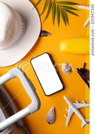 Smartphone with copy space, airplane model, suitcase, sunscreen, straw hat on yellow background 102947389