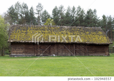 Old Wooden Building With Straw, Thatched Roof In Meadow, Open Air. Bungalow Construction in Rural Eastern Europe Area, Countryside. Horizontal Landscape Plane High quality photo Old Wooden Building With Straw, Thatched Roof In Meadow, Open Air. Bungalow Construction in Rural Eastern Europe Area, Countryside. Horizontal Landscape Plane High quality photo 102948557