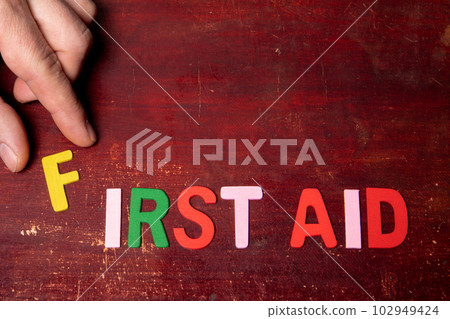 FIRST AID. Text from colored letters on a painted wooden background 102949424