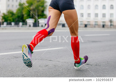 female runner athlete running marathon in city, compression socks on feet, kinesiotaping on knees for prevention 102950837