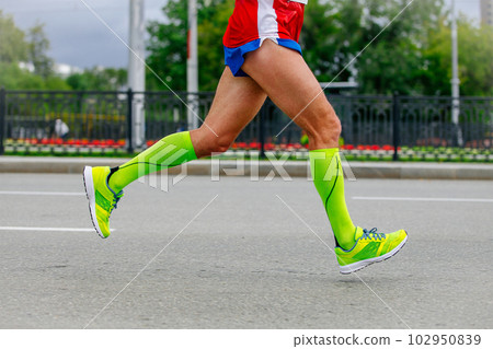 close-up legs runner athlete running marathon in city in green compression socks, sports summer race close-up legs runner athlete running marathon in city in green compression socks, sports summer race 102950839