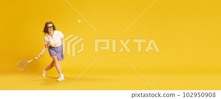 Portrait of young, concentrated girl in sportswear, tennis playing in motion hitting ball with racket against yellow studio background Portrait of young, concentrated girl in sportswear, tennis playing in motion hitting ball with racket against yellow studio background 102950908